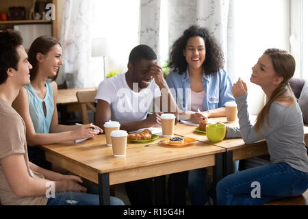 Five diverse student studying together in cafe during lunch, served meal on table coffee tea pastries. Cheerful friends teammates talking share though Stock Photo