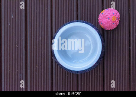 Flat lay image of a dog bowl and pink dog ball on a stained wooden deck Stock Photo