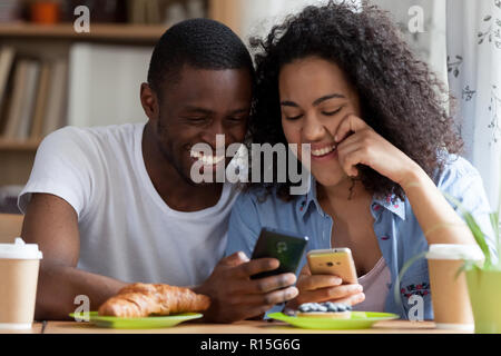 Head shot portrait black guy and biracial girl couple in love sitting together at table in cafe drink coffee eat pastries. Couple using cellular shari Stock Photo