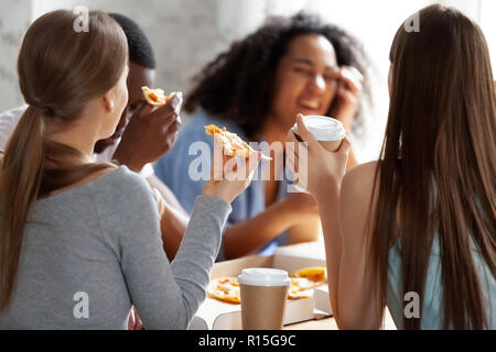 Diverse multi-ethnic best friends meets in pizzeria chatting joking together. Students talking take a break have lunch eating pizza, close up focus on Stock Photo