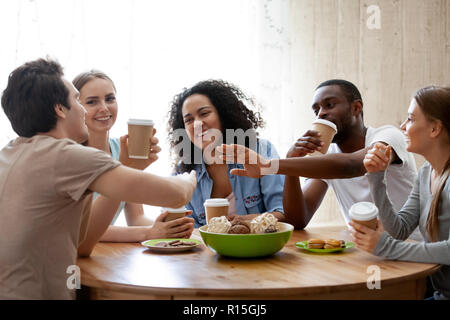 Diverse friends girls and guys sitting around table chatting having fun drink coffee in paper cups enjoy time together. Friendship between different r Stock Photo