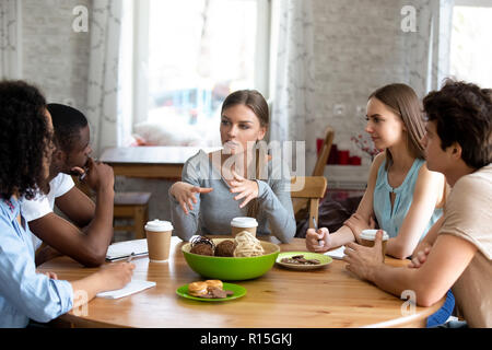 Diverse multi-ethnic students sitting around circle table listen schoolmate ideas studying together in cafe. Multiracial best friends gathered togethe Stock Photo