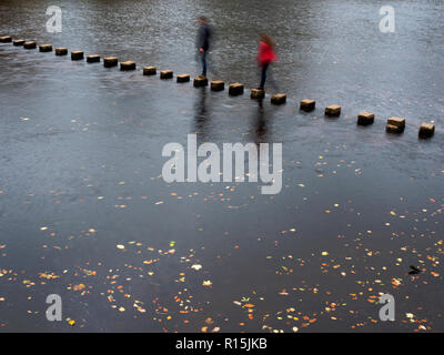 Two blurred figures crossing the stepping stones over the River Wharfe in autumn at Bolton Abbey Yorkshire Dales England
