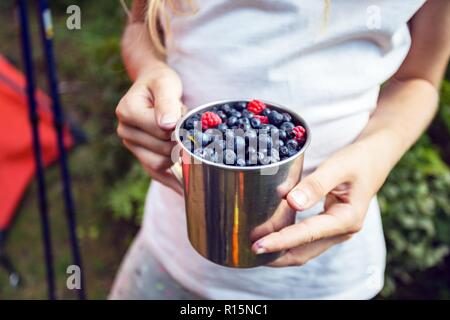 hiking in the mountains. girl holding a cup of raspberries and blueberries on the background of a tent Stock Photo