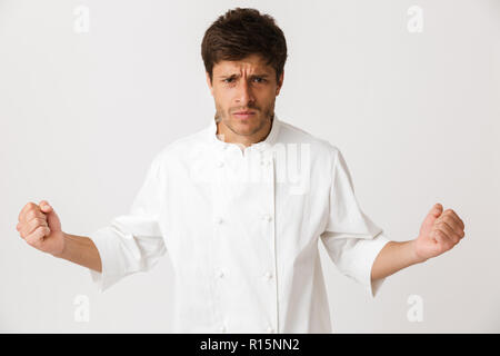 Image of agressive angry young chef man standing isolated over white wall background. Stock Photo