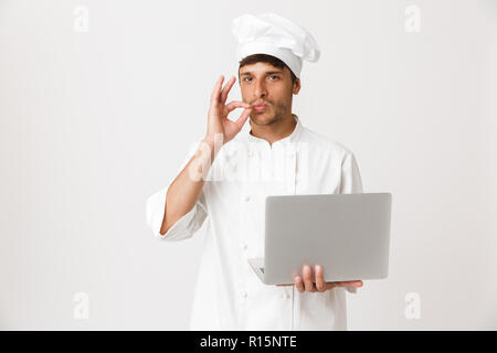 Image of handsome young chef man isolated over white wall background using laptop computer. Stock Photo
