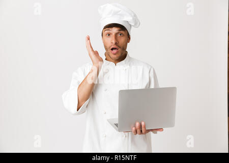 Image of shocked young chef man isolated over white wall background using laptop computer. Stock Photo