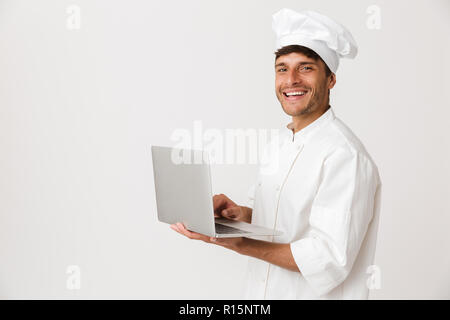 Image of handsome young chef man isolated over white wall background using laptop computer. Stock Photo
