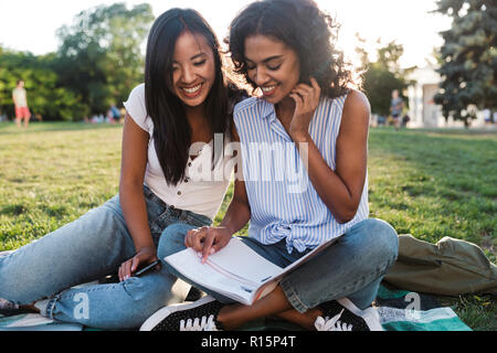 Image of happy smiling young friends girls outdoors in park doing homework. Stock Photo