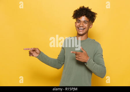 Portrait of teenage african guy having stylish afro hairdo pointing fingers aside at copyspace isolated over yellow background Stock Photo