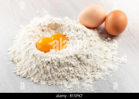 pile of flour with egg yolks for dough on table Stock Photo