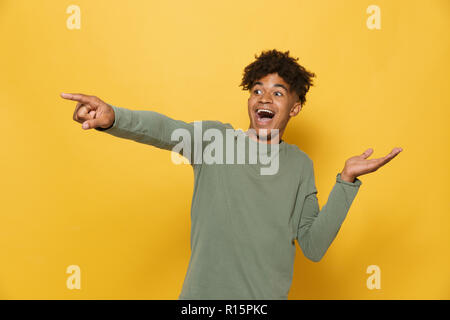 Portrait of happy african guy having stylish afro hairdo pointing fingers aside at copyspace isolated over yellow background Stock Photo