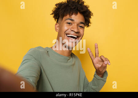 Portrait of funny african man having stylish afro hairdo smiling and taking selfie photo isolated over yellow background Stock Photo