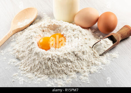 pile of flour with egg yolks and milk bottle on table Stock Photo