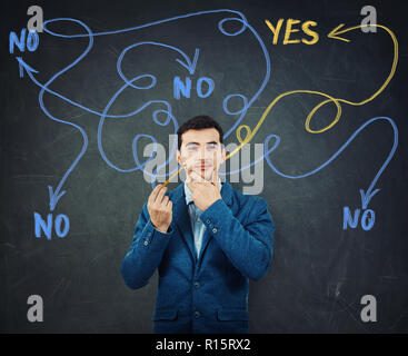 Hard thinking serious smart man hand unde chin over blackboard background finding the answer to questions as curves arrows from head leading to yes or Stock Photo