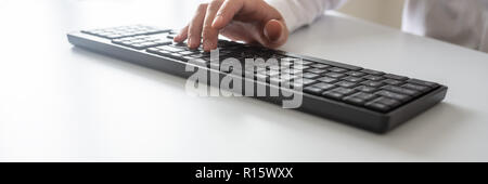 Wide view image of programmer or businessman typing on black computer keyboard using one hand. Stock Photo