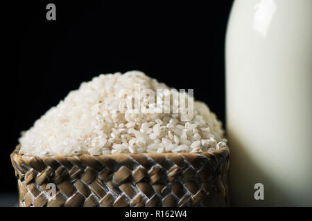 closeup of a basket with rice and a glass bottle with rice milk, against a black background Stock Photo