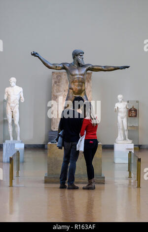 Athens. Greece. Visitors at the National Archaeological Museum of Athens looking at the Artemision Bronze, statue representing Poseidon or Zeus, ancie