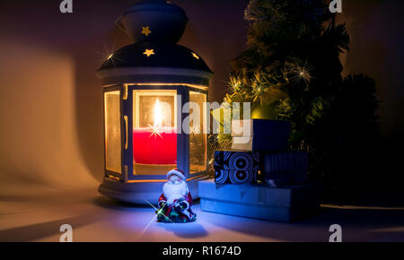 Lantern with burning candle and Christmas tree with gift boxes and Santa Claus with beautiful shadows and with a beautiful shine as a star Stock Photo