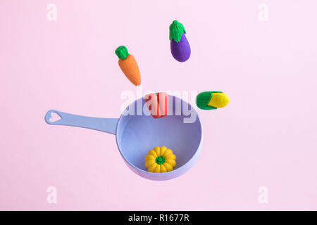 Pan with flying vegetable toys on pastel pink background minimal creative cooking concept. Stock Photo