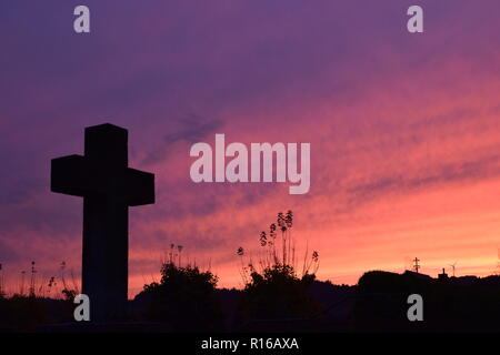 Time-lapse of the setting sun in the evening dusk sky viewed  from behind a red sandstone cross during the setting sun in the civil cemetery Reimsbach Stock Photo