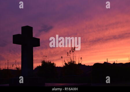 Time-lapse of the setting sun in the evening dusk sky viewed  from behind a red sandstone cross during the setting sun in the civil cemetery Reimsbach Stock Photo