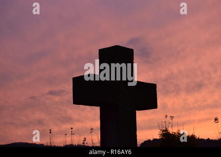 Time-lapse of the setting sun in the evening dusk sky viewed  from behind a red sandstone cross during the setting sun in the civil cemetery Reimsbach Stock Photo