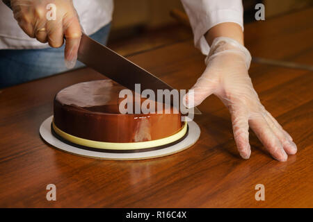 Prague mousse cake. Woman cuts off a piece of cake with a kitchen knife. Cooking in a pastry shop. Stock Photo