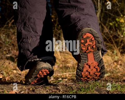 Hikers boots on forest trail. Autumn hiking. Close-up of walking in trekking shoes on the background of leaves and trees. Stock Photo