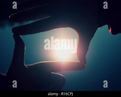 Hands catch sun at sunset time. Female fingers hold sun above lake level. Stock Photo