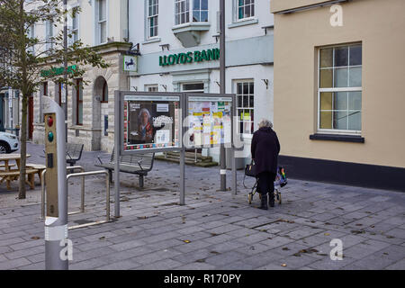 Older woman using a walker passes the town notice board at Castletown, Isle of Man Stock Photo