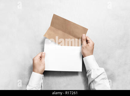 Hand holding white blank envelope and folded craft leaflet mockup, isolated. Arm hold empty brochure template mock up. Greeting card flyer design. Inv Stock Photo