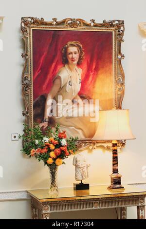 Beautiful portrait painting of Lady Iliffe hanging up in Basildon Park (National Trust) with lamp and a vase of flowers beside Stock Photo