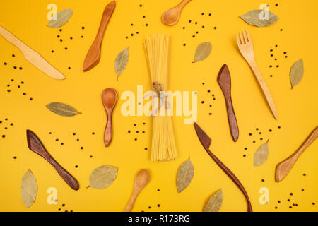 Handcrafted wooden utensils, pasta and spices. Flat lay composition on bright yellow background. Stock Photo
