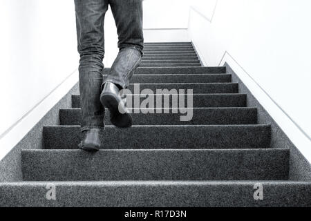 Black and white low angle picture of one man walking upstairs on staircase indoors Stock Photo