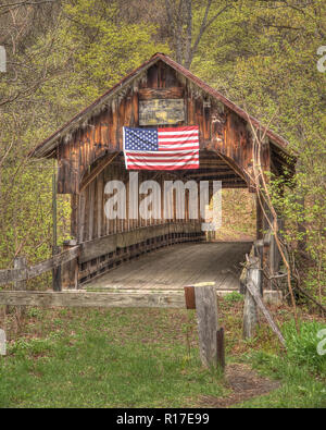 An abandoned covered bridge proudly fly's the American Flag on its weathered wood design in the early fall. Stock Photo