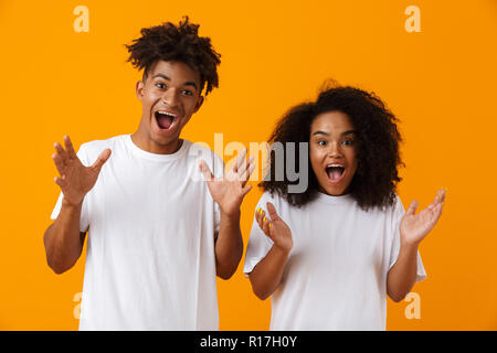 Image of excited emotional young cute african couple posing isolated over yellow background. Stock Photo