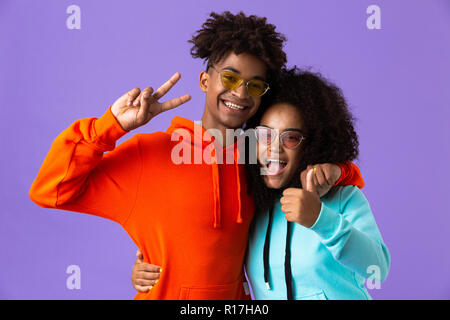 Image of happy young cute african couple posing isolated over violet background showing peace gesture hugging. Stock Photo