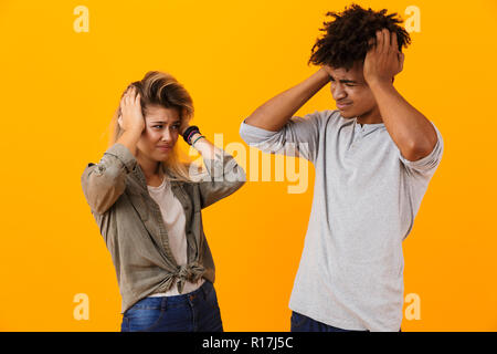 Portrait of a shocked multiethnic couple standing isolated over yellow background, looking at each other Stock Photo