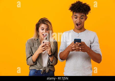 Image of happy cute young loving couple posing isolated over yellow background using mobile phones. Stock Photo