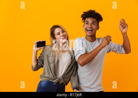 Photo of happy young loving couple dancing isolated over yellow background listening music by earphones. Stock Photo