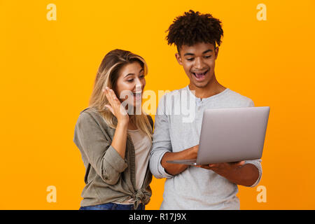 Photo of happy young loving couple standing isolated over yellow background using laptop computer. Stock Photo