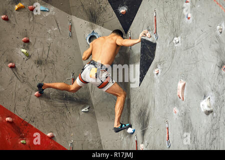 Male climber exercising in gym, climbing up on artificial wall with boulders. Stock Photo
