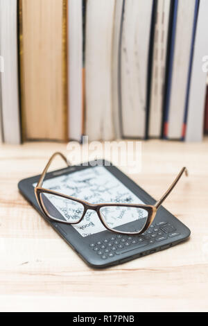 The glasses are lying on the book reader. Traditional books in the background Stock Photo