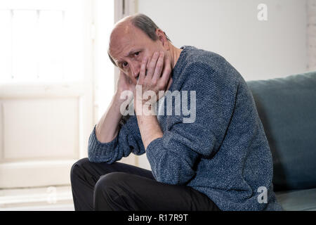 Overwhelmed old senior man suffering alone at home feeling confused sad alone on couch at home in Aging Retirement widower Dementia and Alzheimer conc Stock Photo