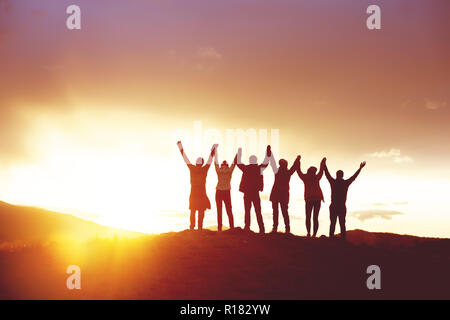 Big group of happy friends with raised hands at sunset. People's silhouettes. Unity, success, team or friendship concept Stock Photo