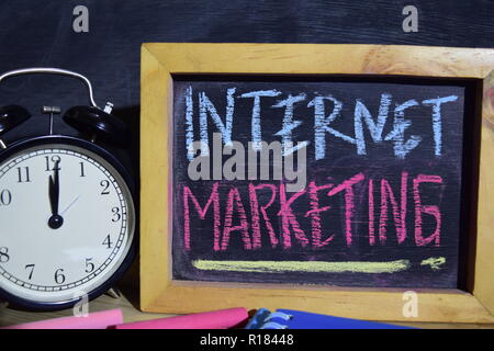 Internet marketing on phrase colorful handwritten on blackboard. Education and business concept. Alarm clock, chalk, books on black background Stock Photo