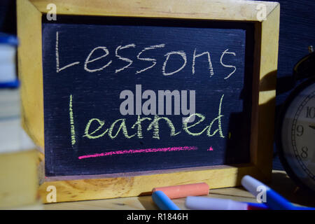 Lesson learned on phrase colorful handwritten on blackboard. Education and business concept. Alarm clock, chalk, books on black background Stock Photo