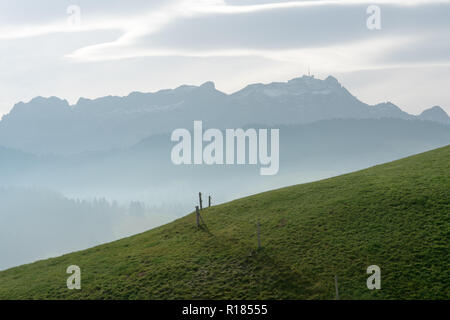 idyllic and peaceful mountain landscape with a wooden fence on a grassy hillside and a great view of the Swiss Alps behind Stock Photo