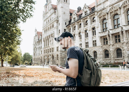 A tourist man or boy with a backpack or a student in Leipzig in Germany uses a mobile phone to view a map or call or for another. Stock Photo